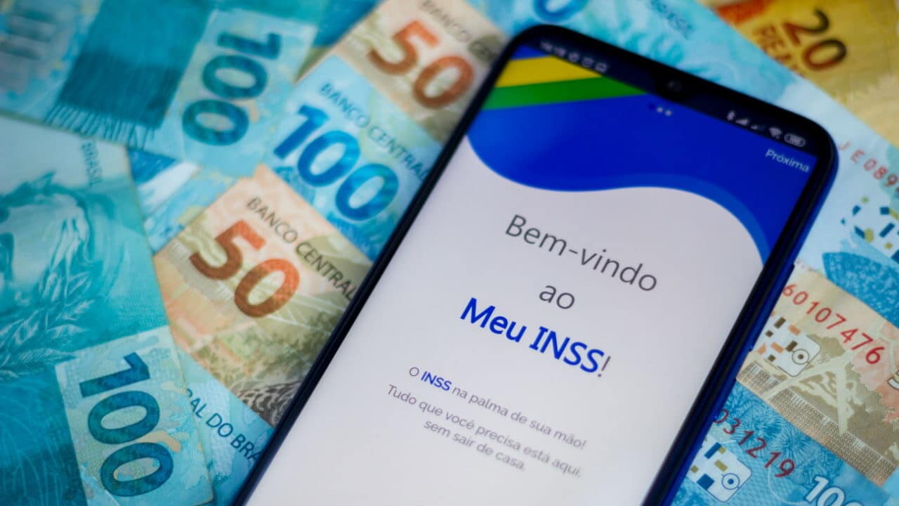 Celular com aplicativo Meu INSS sobre notas de 50 e 100 reais