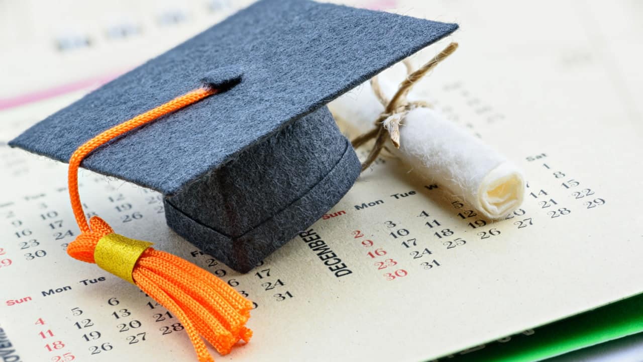 Miniaturas de um capelo de formatura e um diploma sobre uma página de calendário.