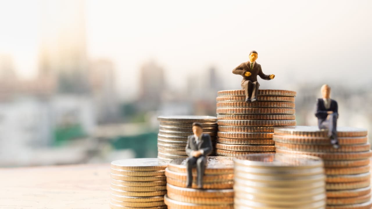 Miniaturas de empresários sentados em pilhas de moedas com tamanhos diferentes, conceito de desigualdade financeira.