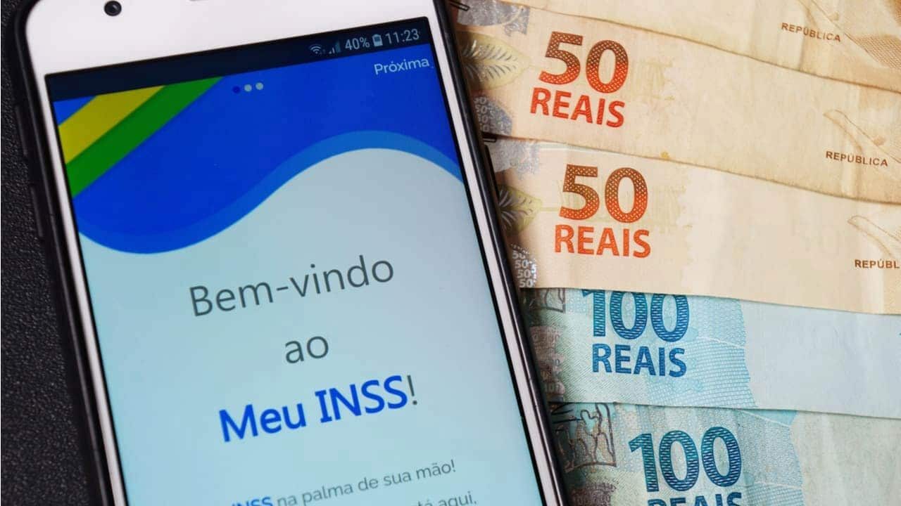 Ao lado de notas de 50 e 100 reais, celular exibe tela inicial do aplicativo do Meu INSS