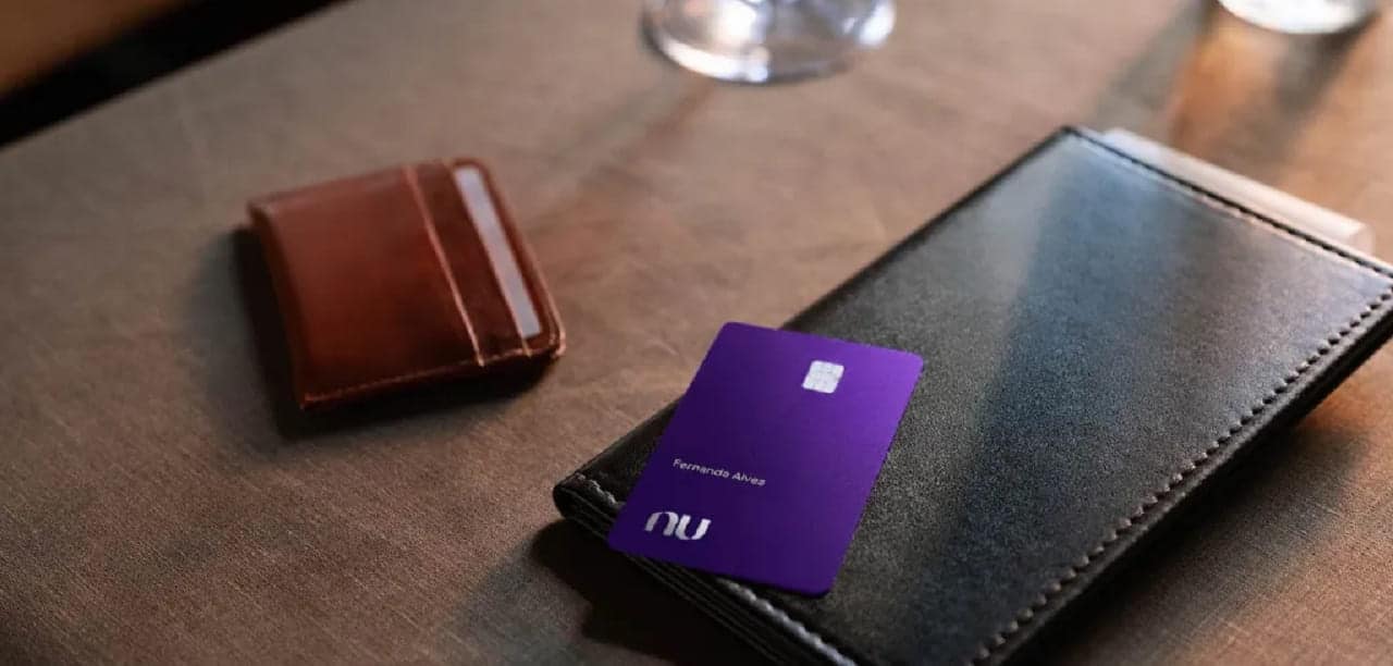 Em uma mesa estão um celular, uma carteira e um cartão Ultravioleta do Nubank
