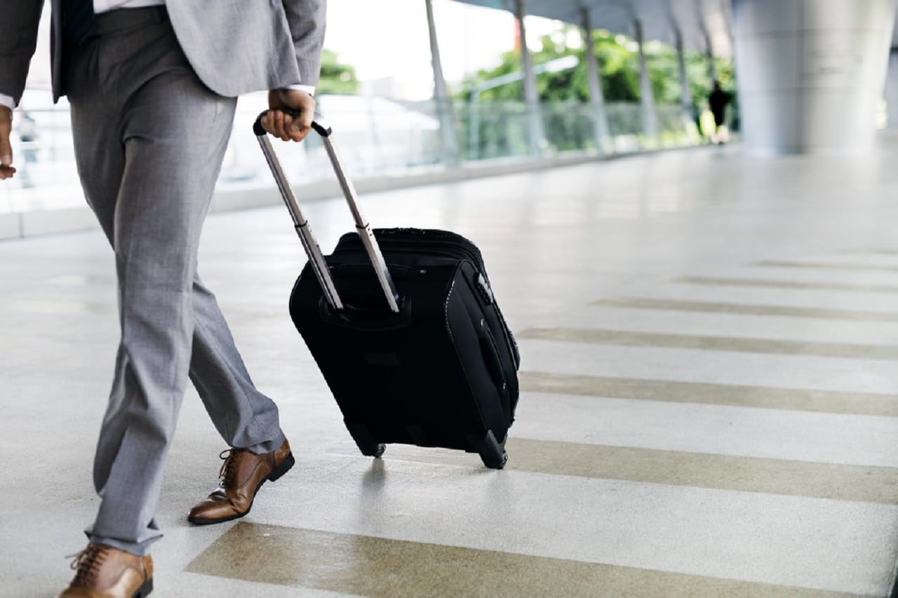 Imagem de um profissional carregando uma mala de rodas na cor preta em viagem a trabalho.