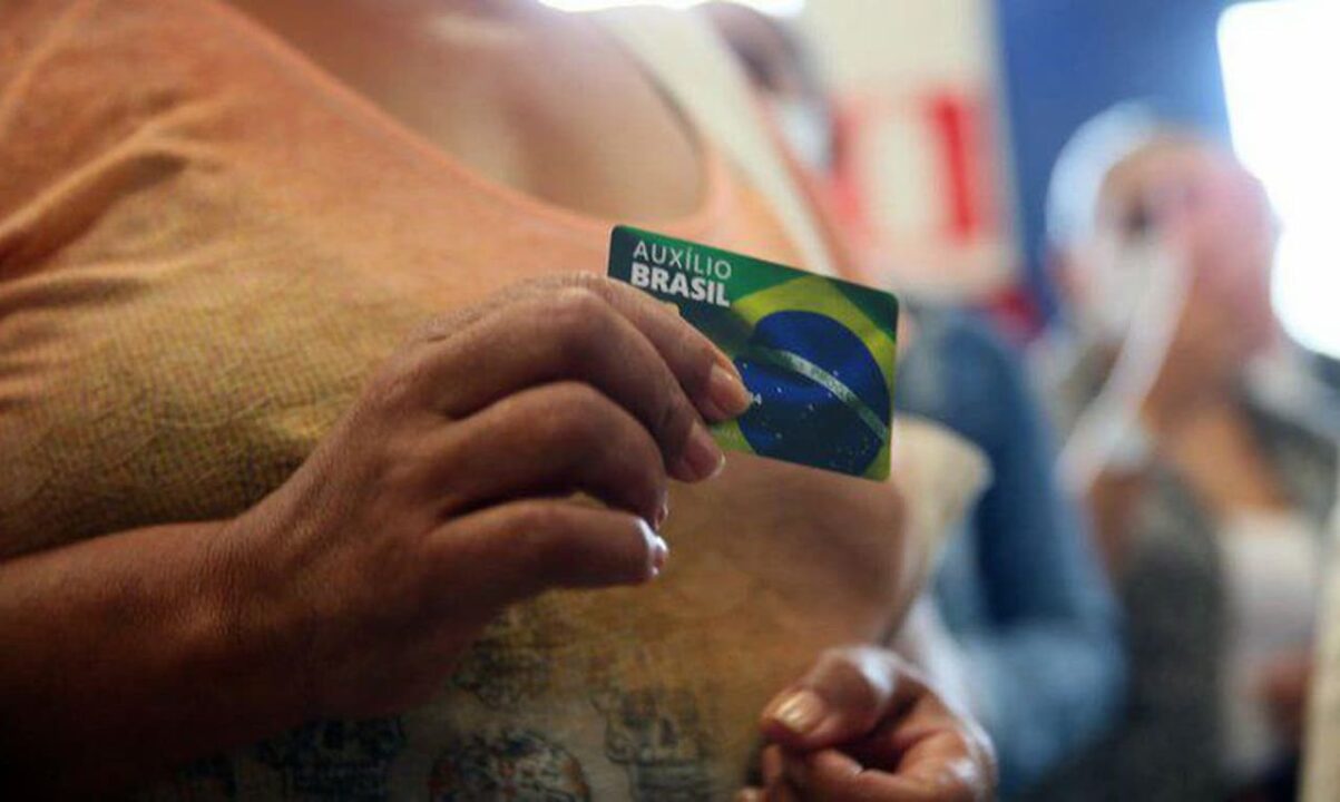 mulher com cartão do Auxílio Brasil em mãos