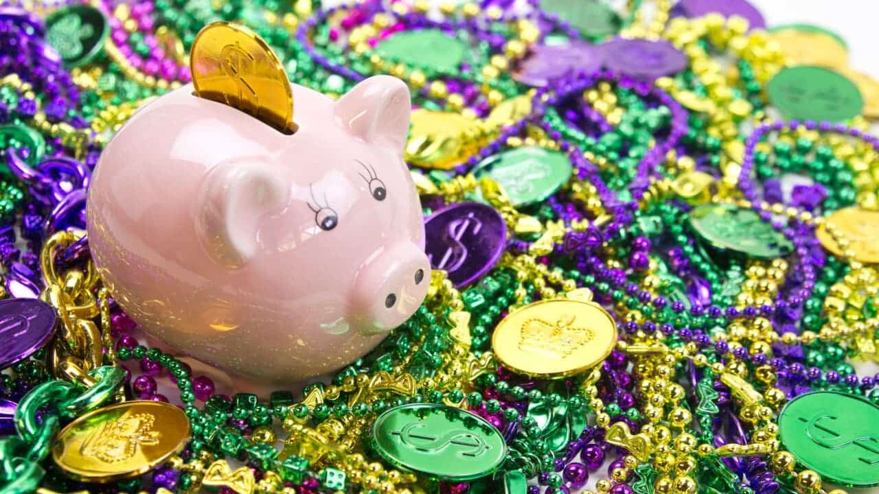 Imagem de cofrinho em formato de porco com uma moeda posicionada na abertura. À sua volta, várias moedas coloridas e acessórios de Carnaval.