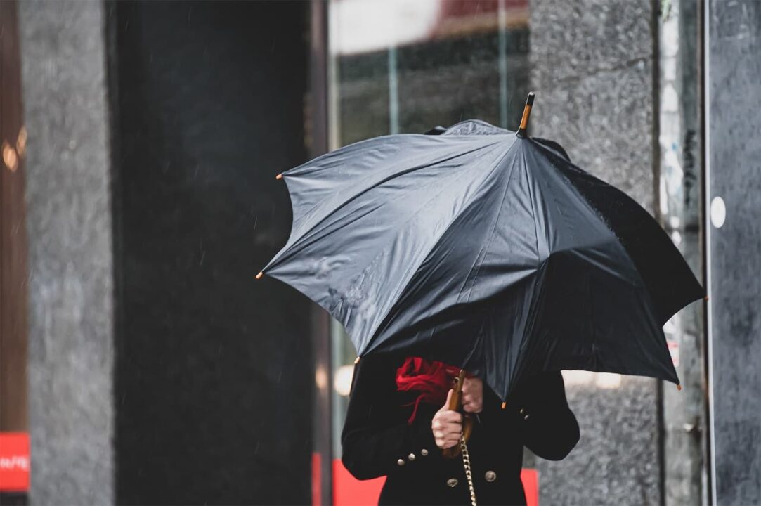Uma mulher tem dificuldade em segurar um guarda-chuva devido a ventos fortes em tempo chuvoso