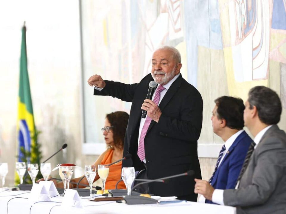 Lula fazendo um discurso de pé ao lado de outros executivos crédito