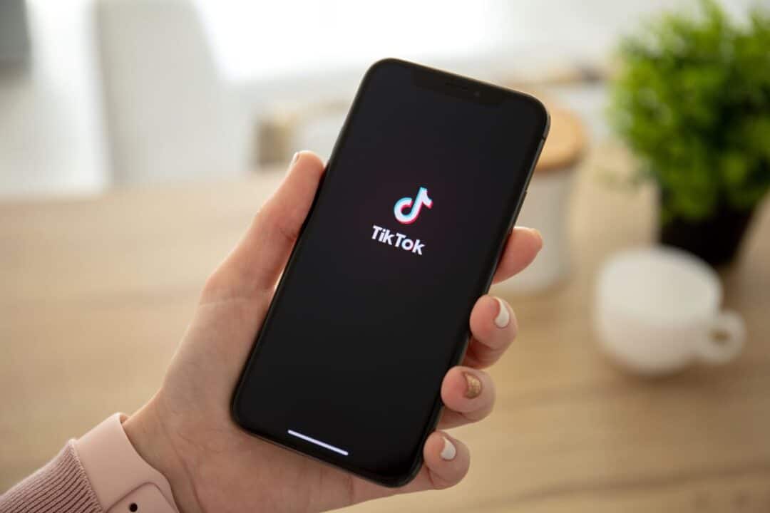 Mão segurando celular que exibe na tela a logo do TikTok