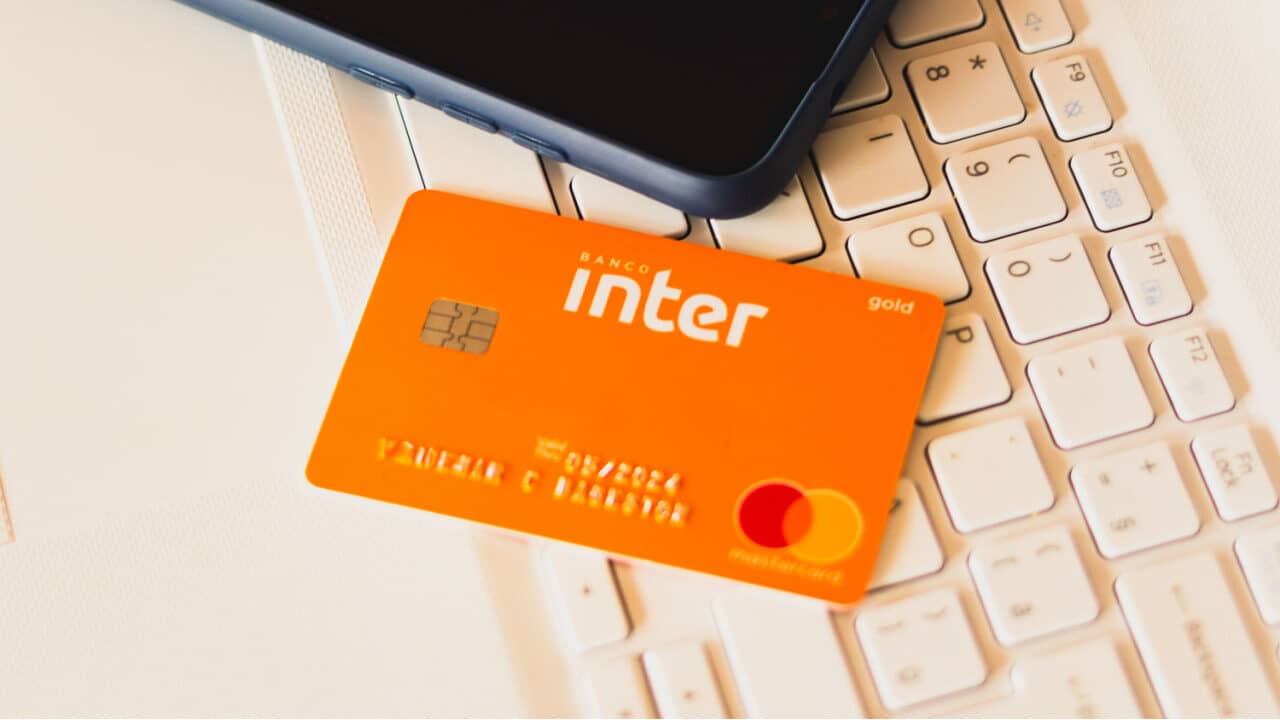 Cartão de crédito do Banco Inter ao lado de um celular. Os dois objetos estão sobre um teclado de computador.