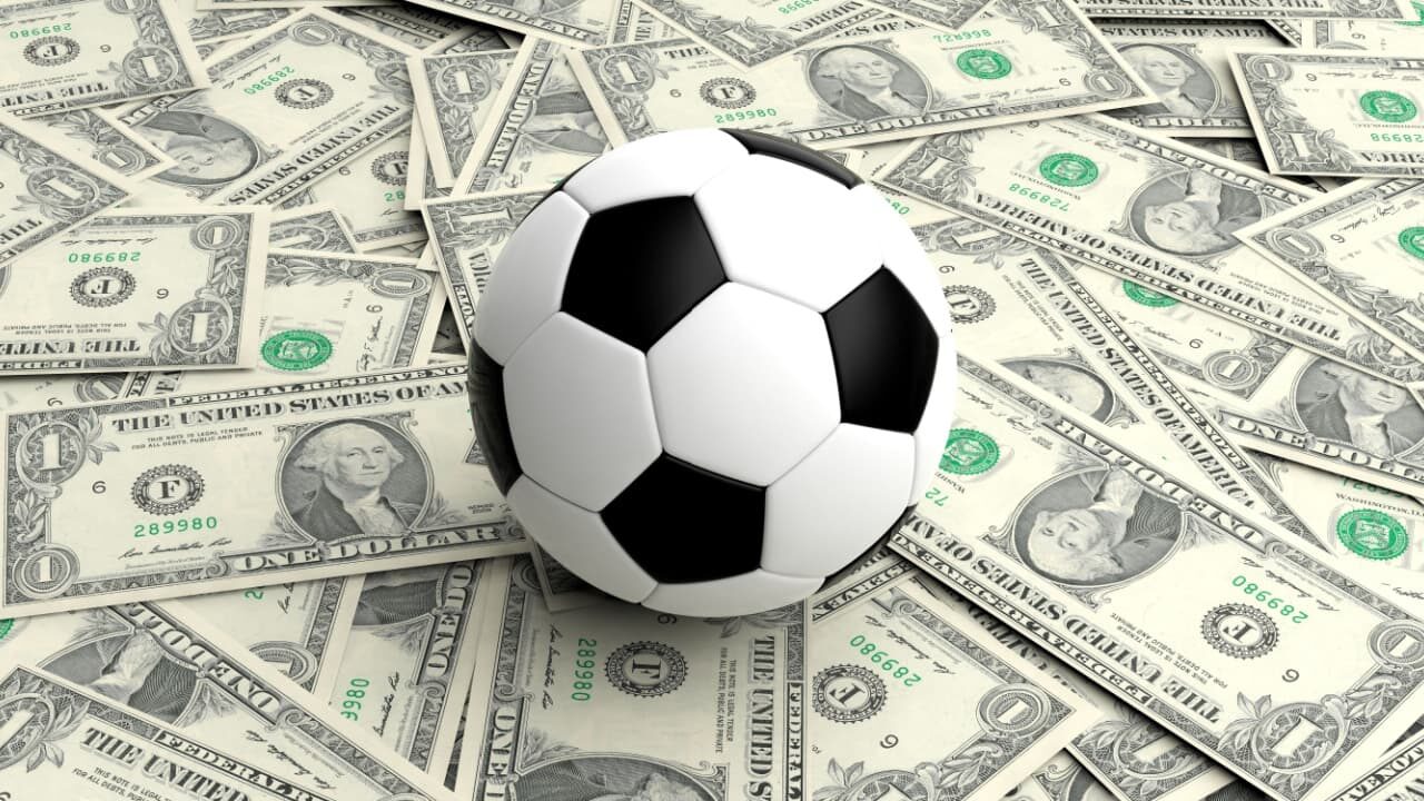 Bola de futebol posicionada sobre várias notas de dólar espalhadas