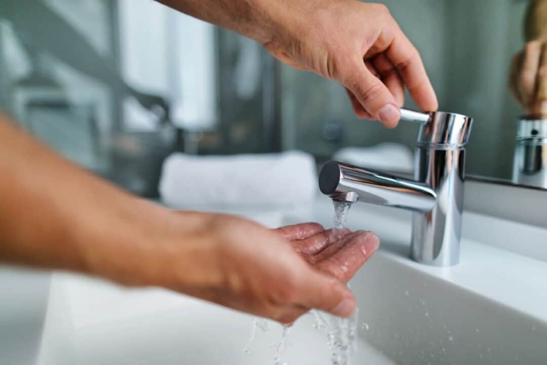a mão de uma pessoa abrindo uma torneira enquanto a pessoa lava a outra mão