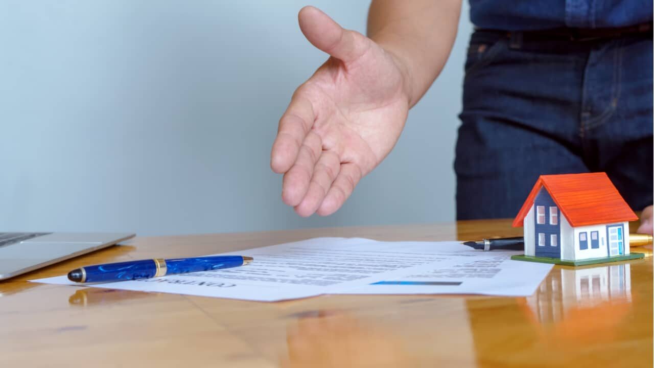 mão apontando documento em cima de uma mesa ao lado de uma caneta
