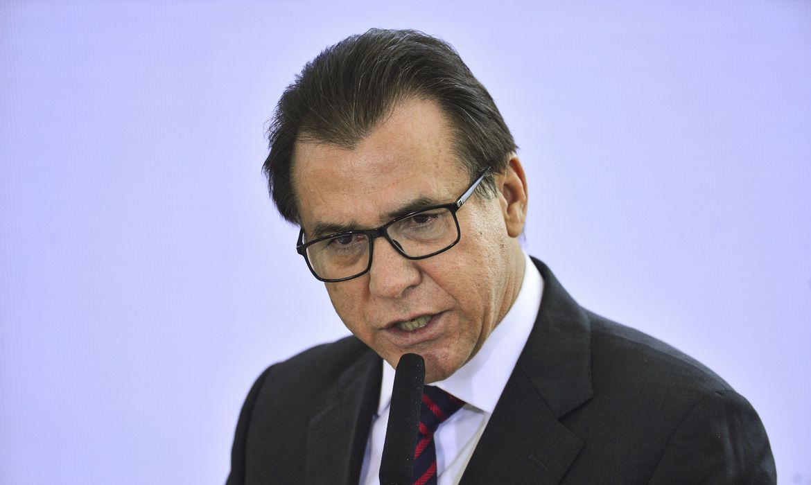 Ministro do Trabalho, Luiz Marinho, durante uma fala atrás de um microfone, representando decisão do governo.