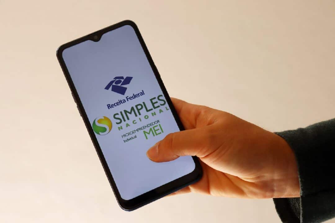 Imagem de uma pessoa utilizando um celular com a tela na logo do MEI.
