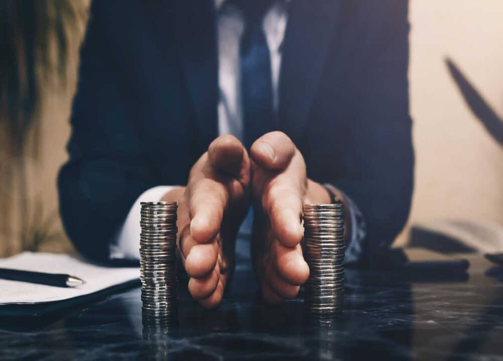 Homem de terno preto separando duas torres de moedas com as mãos sobre uma mesa