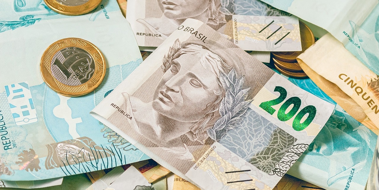 Imagem mostra diversas notas e moedas do real, espalhadas em uma mesa.