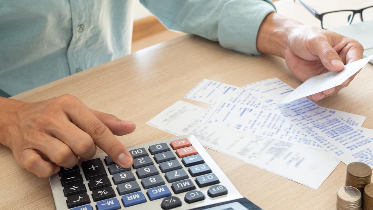 Pessoa realizando contas com calculadora e extratos ao lado