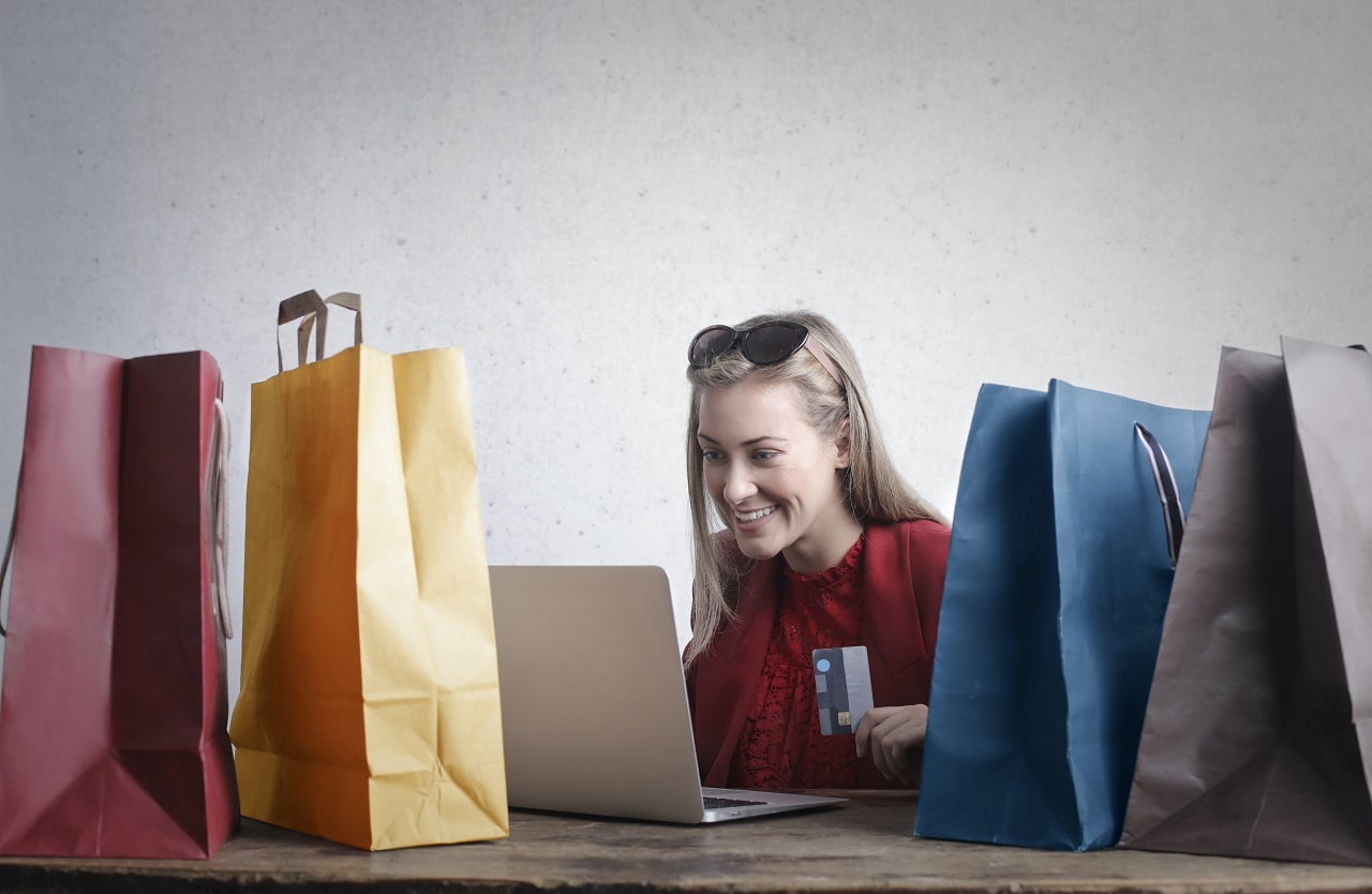Imagem mostra mulher fazendo compras no computador enquanto está rodeada de sacolas.