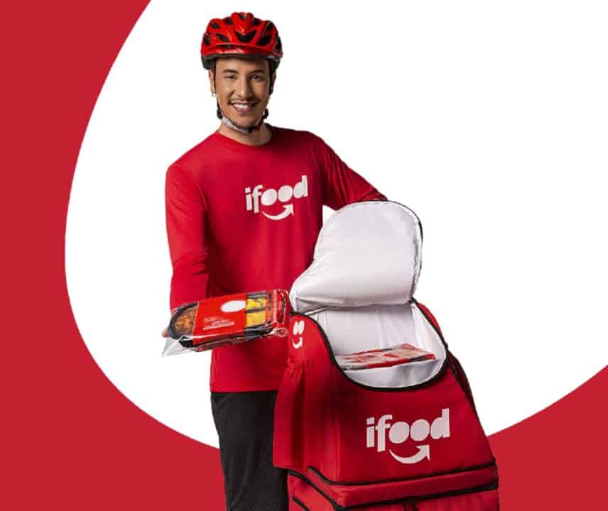 Imagem mostra um entregador do iFood segurando um pedido com a mochila aberta e sorrindo.
