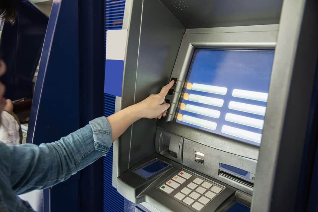 Mão feminina apertando botão em caixa eletrônico para saque FGTS