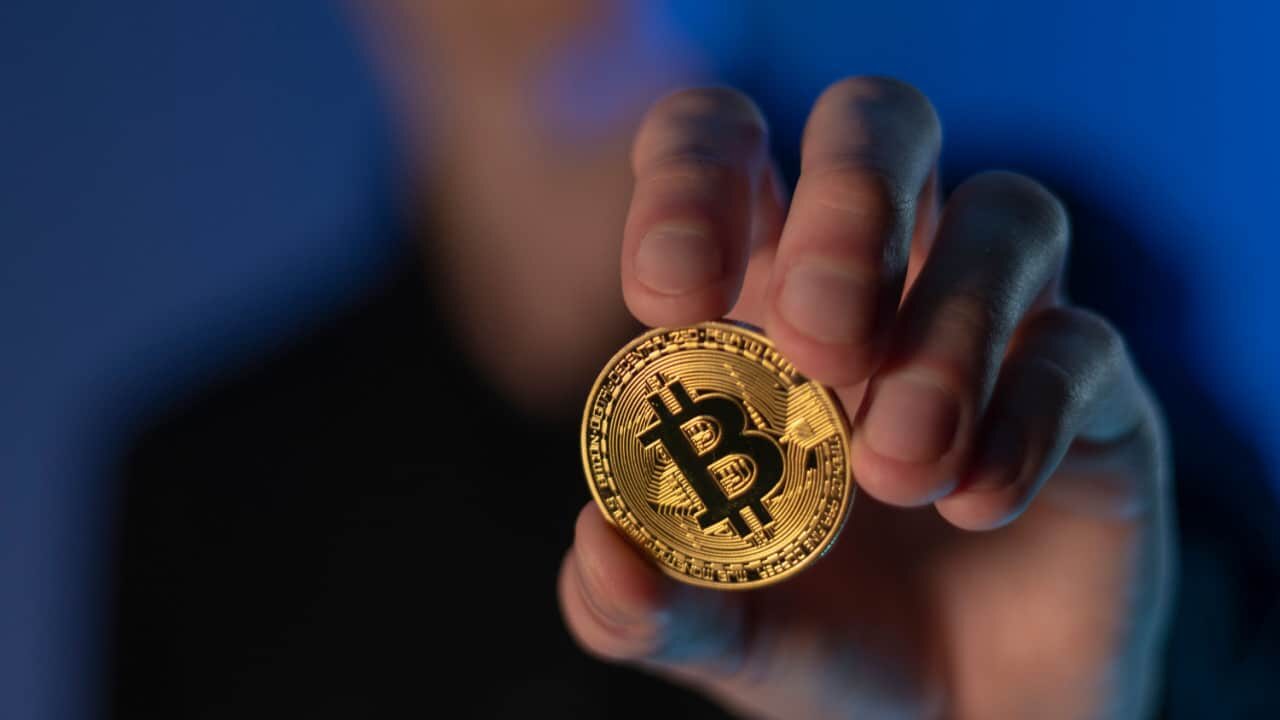 Pessoa com rosto desfocado segurando moeda de Bitcoin