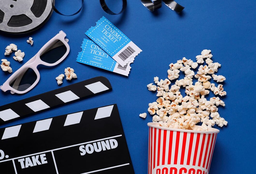 Óculos de cinema, balde de pipoca, claquete e óculos espalhados sobre um fundo azul