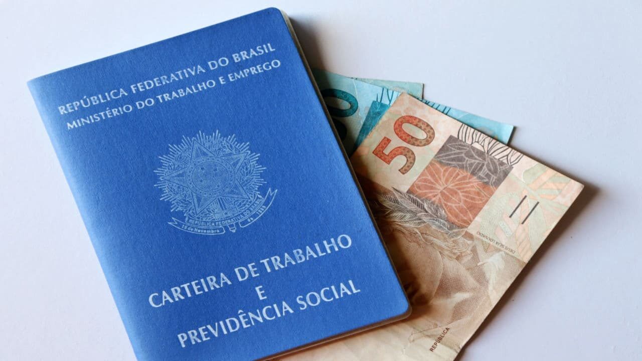 Carteira de trabalho com cédula de 50 e 100 reais ao fundo