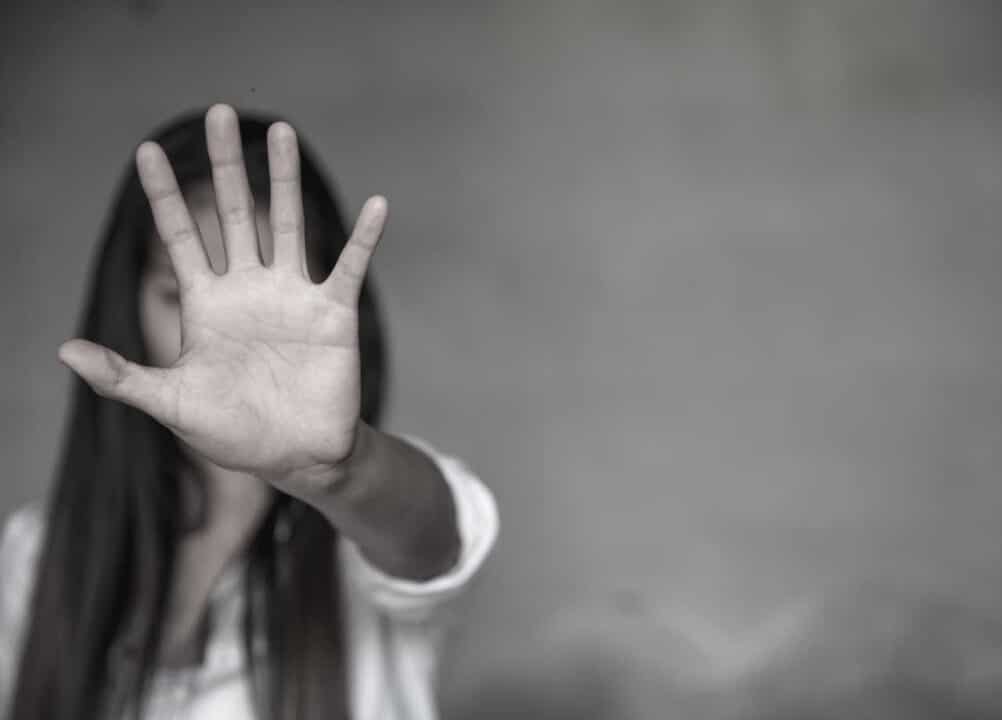 Uma mulher com a mão em frente ao rosto para impedir violência contra as mulheres