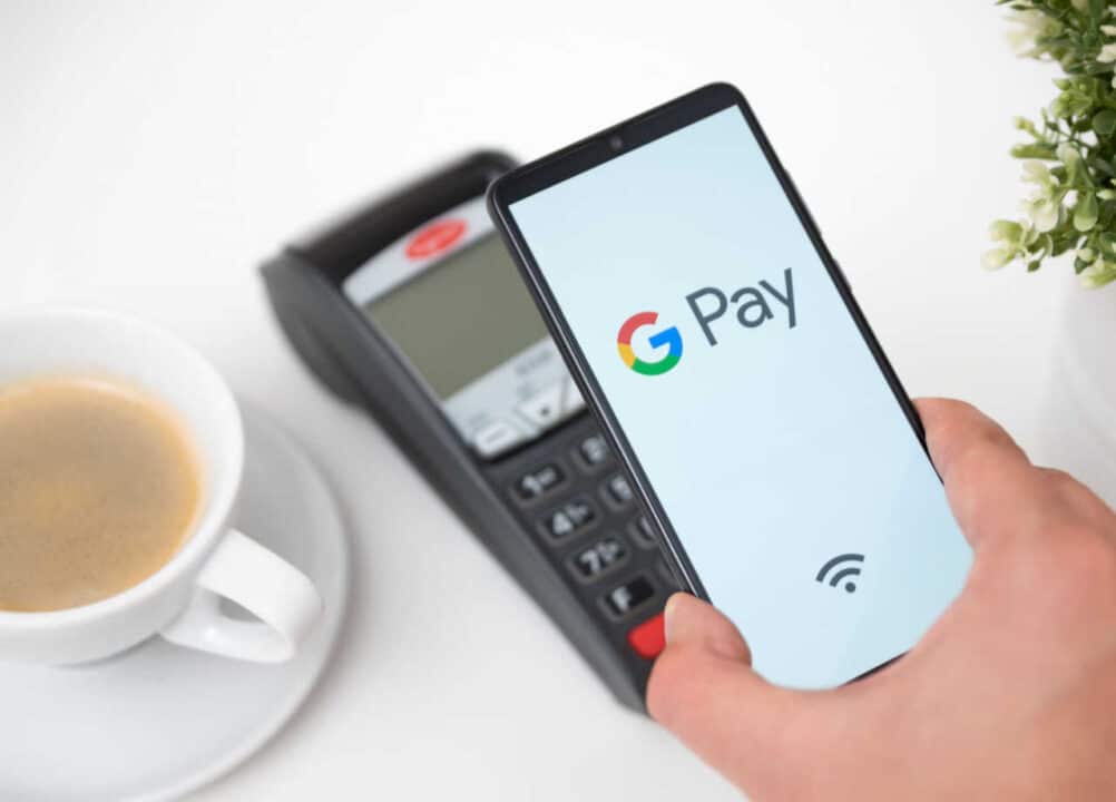 Pessoa usando o Google Pay para pagar algo em uma máquina de cartão ao lado de um café