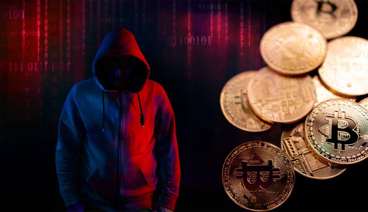 imagem escura de um hacker usando capuz de pé ao lado de um amontoado de moedas douradas da criptomoeda bitcoin