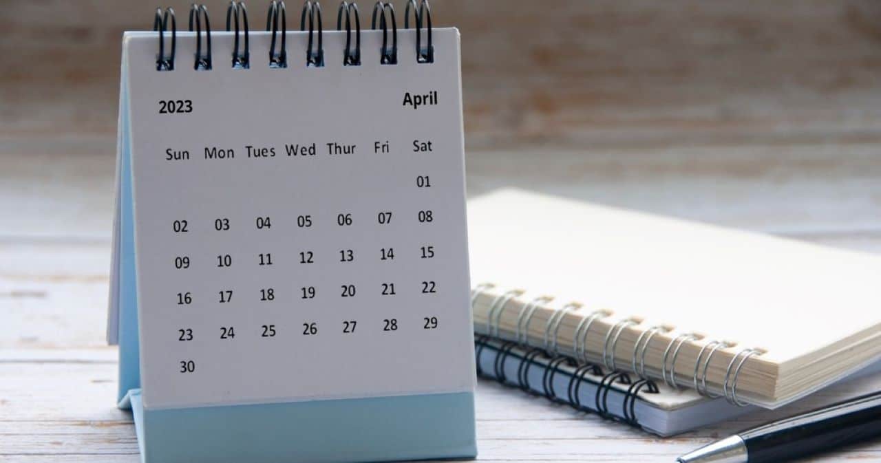 calendário com a página do mês de abril de 2023 em cima da mesa com uma agenda e uma caneta do lado