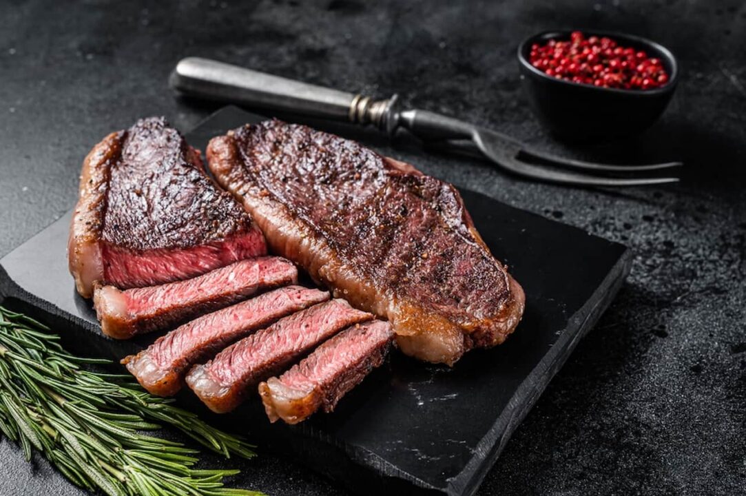 Carne fatiada sobre granito, ao lado de um garfo e temperos
