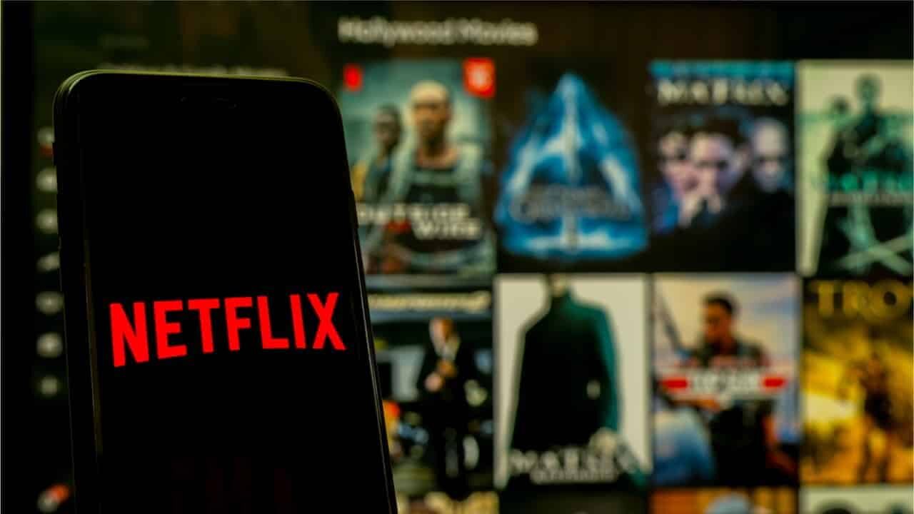 Celular com logo Netflix e filmes ao fundo, em uma tela maior