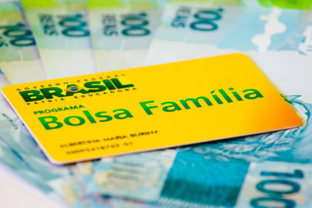 Imagem de um cartĂŁo do Bolsa FamĂlia sobre vĂĄrias notas de R$100 em formato de leque