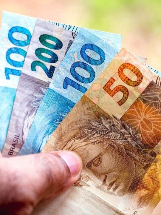 Mão segurando notas de R$50, R$100 e R$200