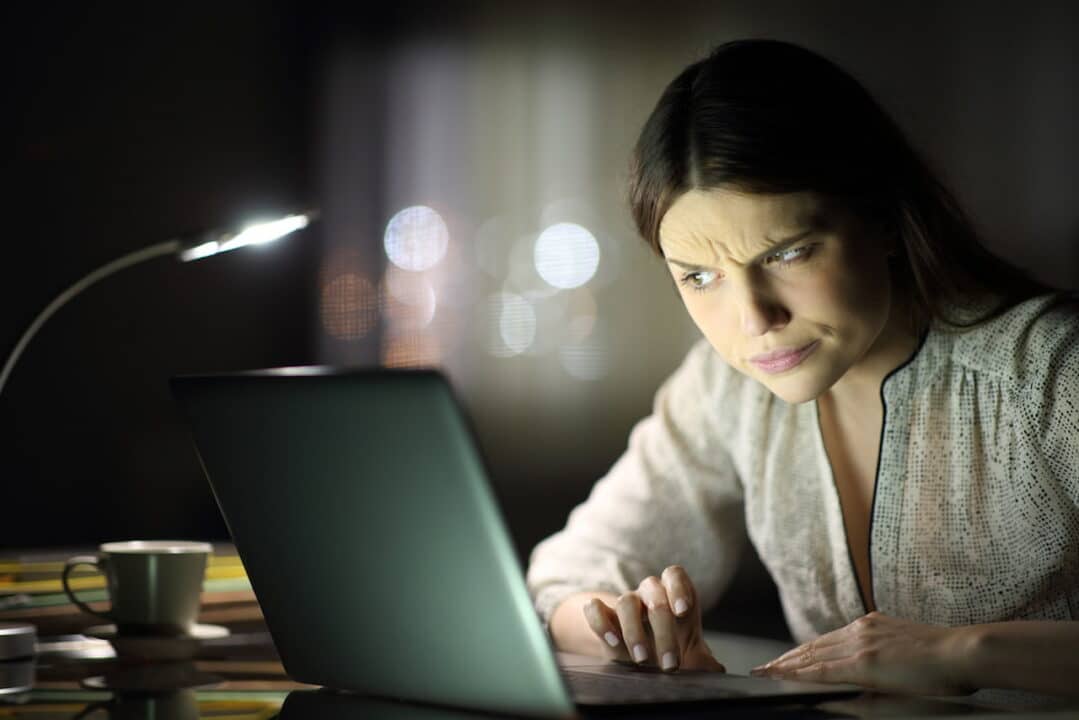 Mulher olhando para um notebook com expressão de desconfiada