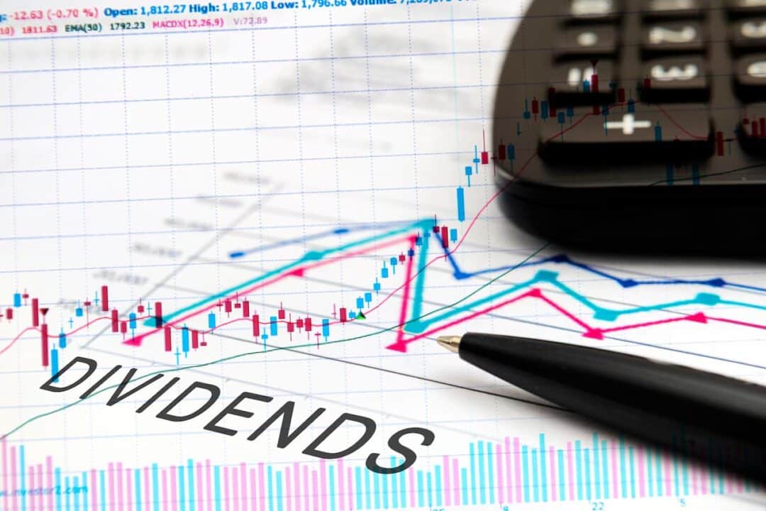 Um mapa com gráficos escrito "dividends", a ponta de uma caneta e calculadora, em cima da folha.