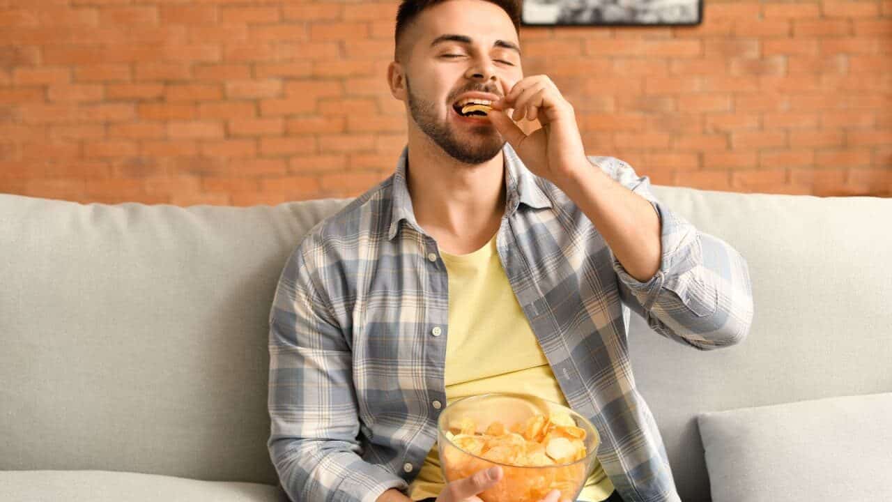 home sentado em sofá comendo batatas dentro de uma tigela