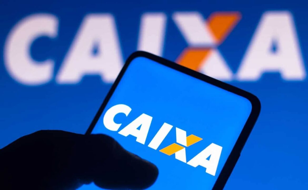 Mão segurando celular com aplicativo da Caixa aberto e logo da caixa ao fundo