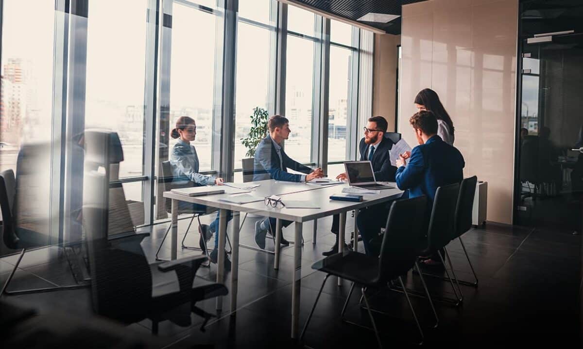 Imagem de diversas pessoas, entre homens e mulheres, em uma mesa, fazendo uma reunião.