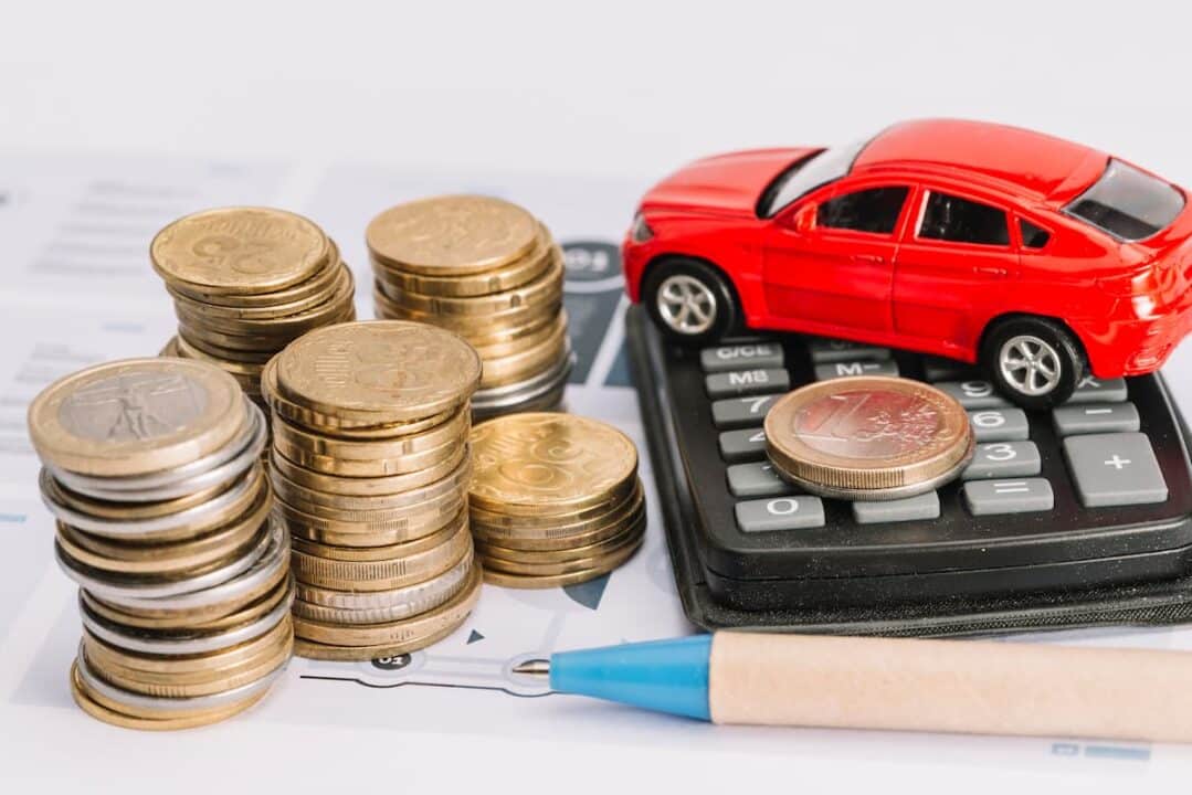 pilha de moedas ao lado de um carro vermelho de brinquedo e uma caculadora ipva