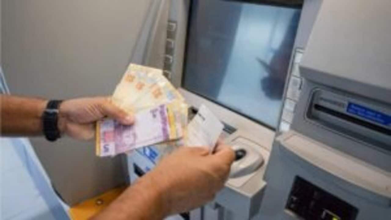 Mãos de uma pessoa sacando notas de dinheiro em um caixa eletrônico de banco