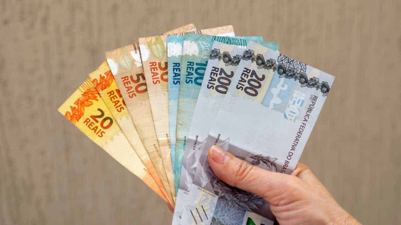 Mão segurando, em formato de leque, notas de 20, 50, 100 e 200 reais