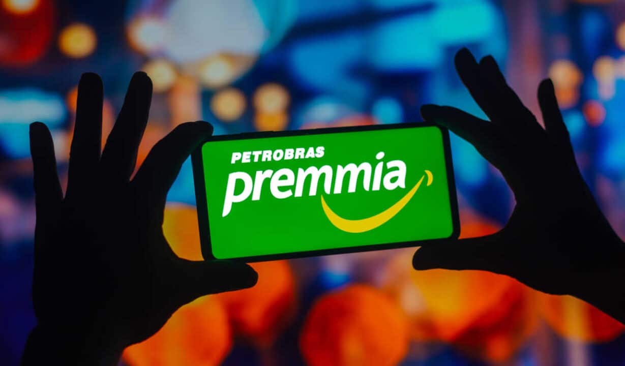 Pessoa segurando celular com as pontas dos dedos e a logo do Petrobras Premmia na tela