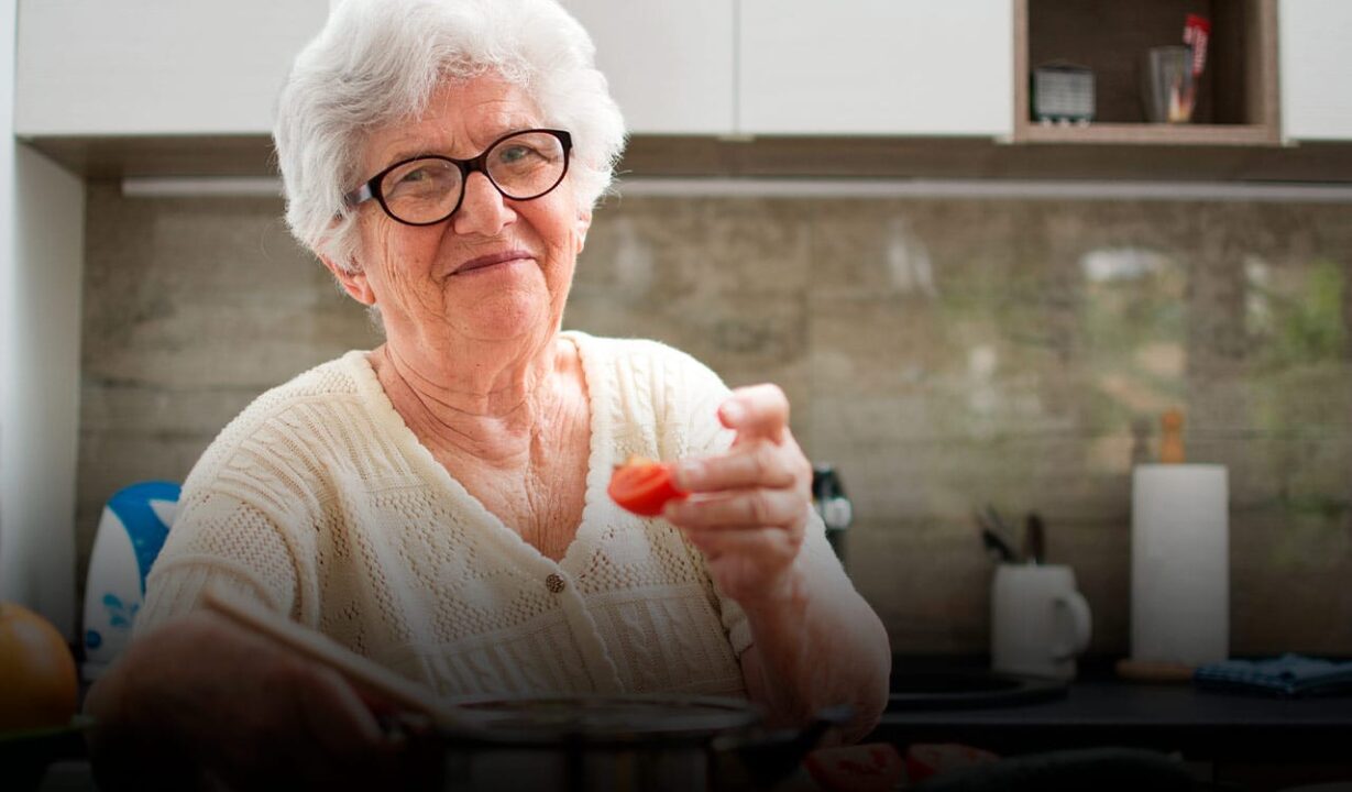 imagem de uma idosa dona de casa sorrindo enquanto segura um copo