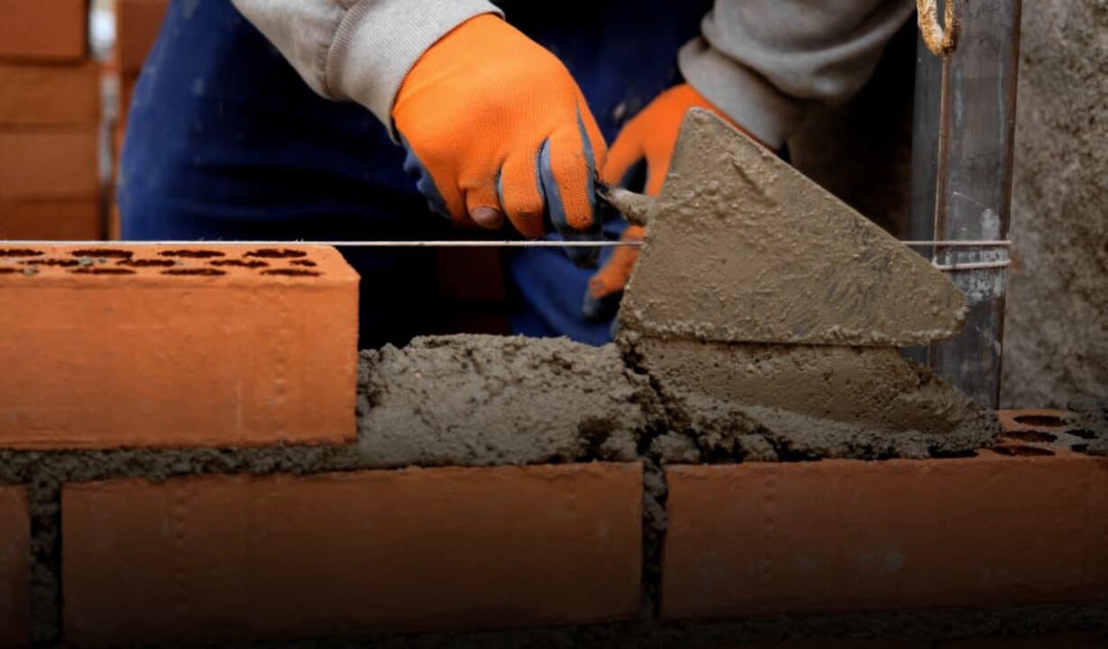 Profissional da construção civil colocando cimento em tijolos laranjas