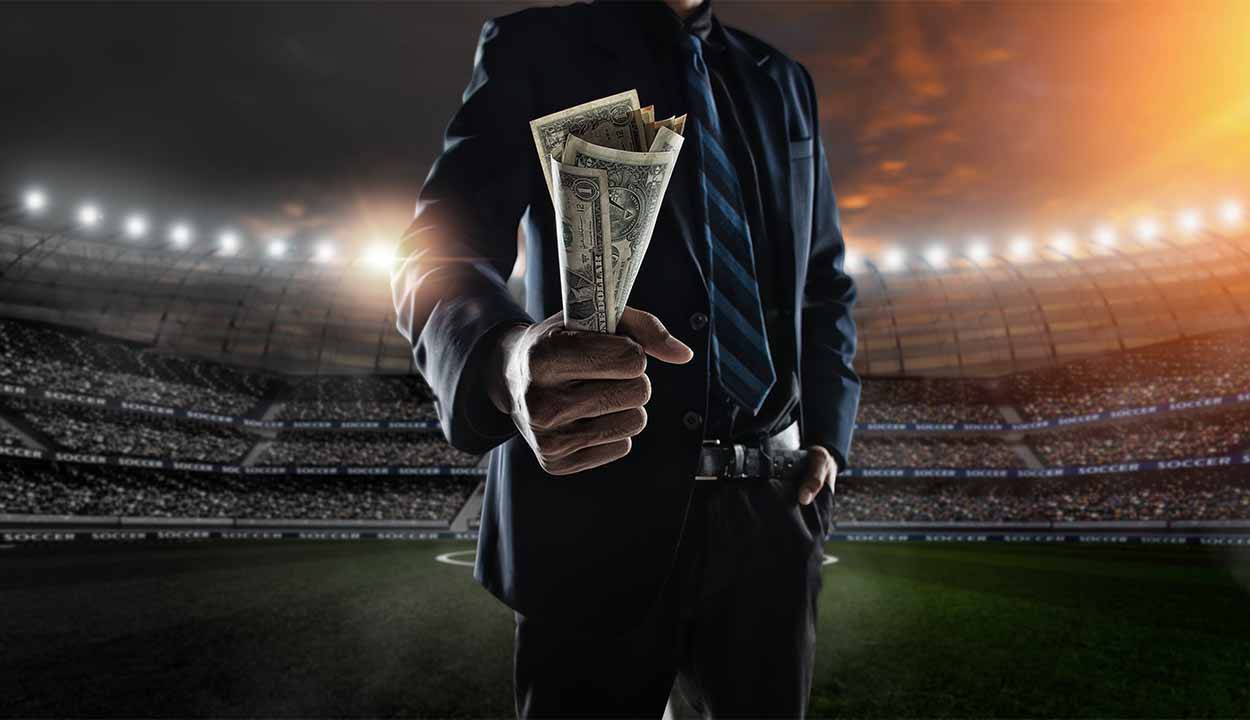 Homemde terno em um campo de futebol segurando cédulas de dólar