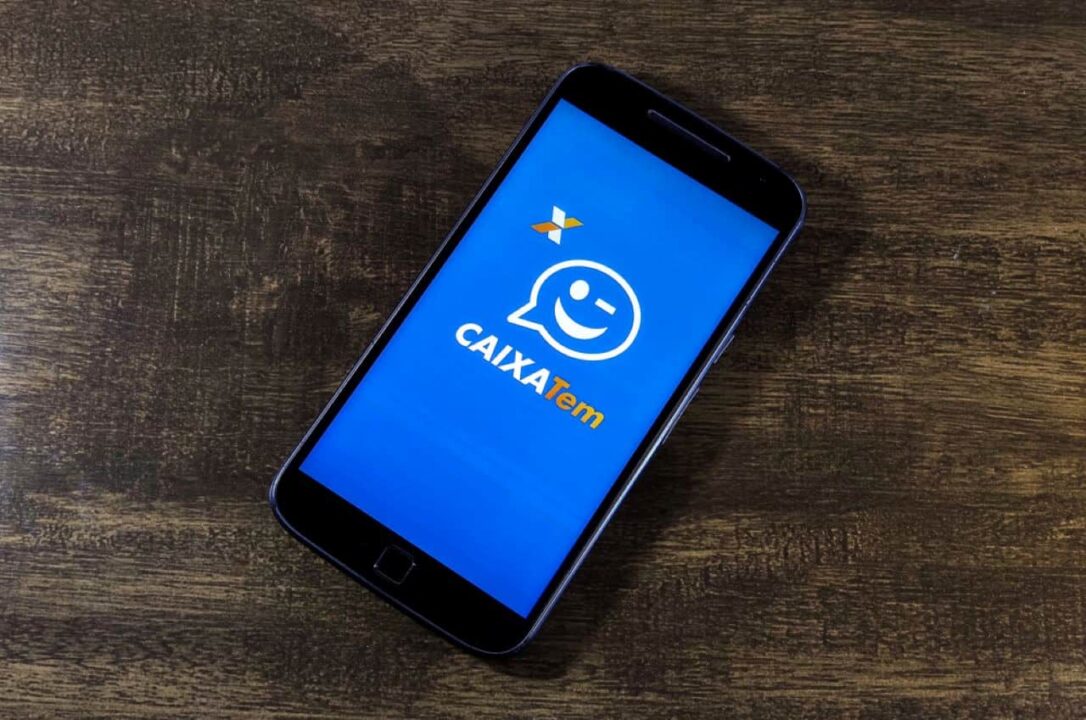 Posicionada em uma superfície escura, celular exibe tela inicial do aplicativo Caixa Tem