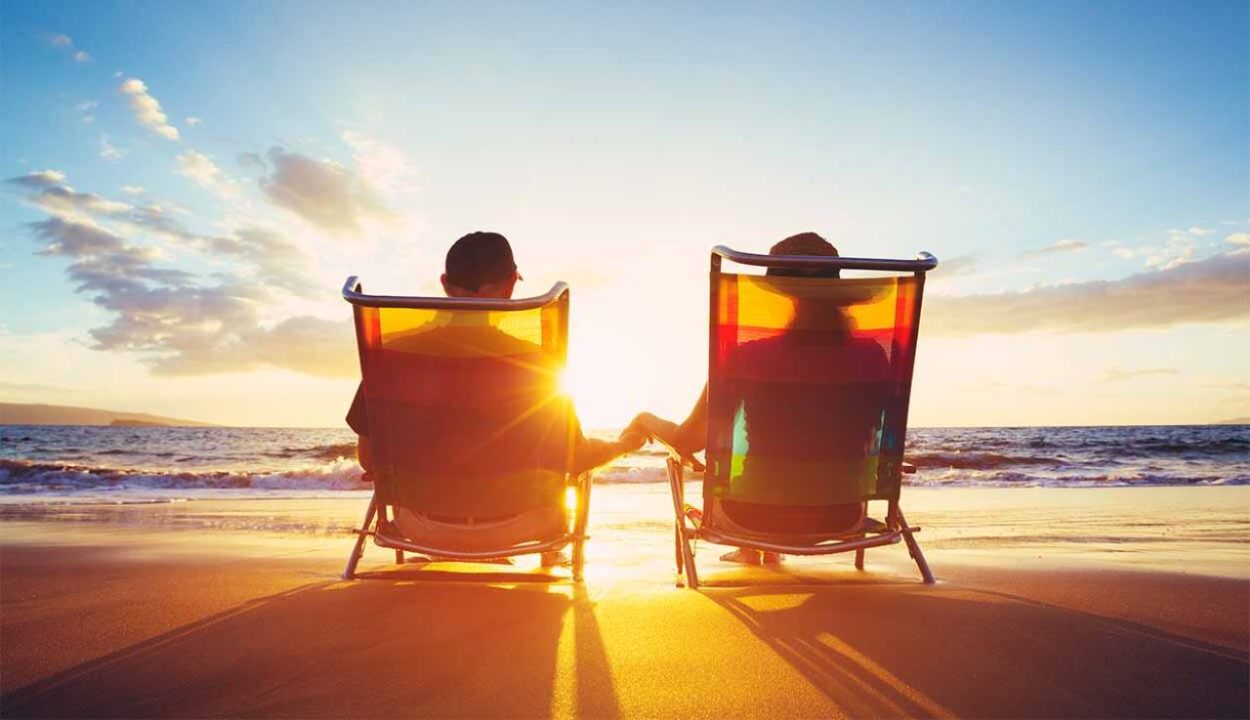 casal de aposentados sentado na cadeira da praia admirando o pôr do Sol