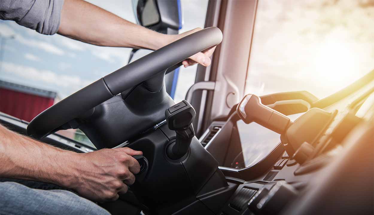 A imagem mostra duas mão segurando um volante de caminhão dirirgir