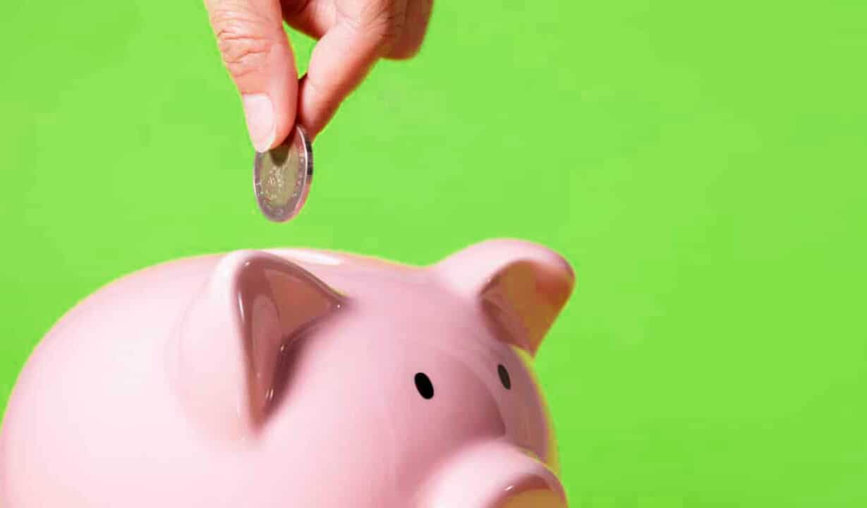 Cofrinho de porquinho rosa simbolizando economia, enquanto uma pessoa adiciona uma moeda no cofrinho. deserdar